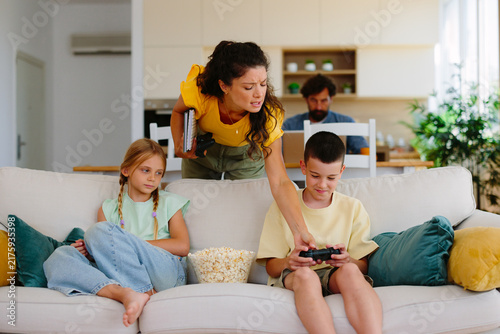 Bild auf Leinwand Mother feeling frustration while interrupting her children's gaming session on t