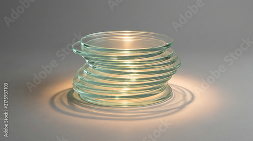 Petri Dish Stack: A precise stack of clean, clear glass petri dishes, illuminated by a soft, warm light that casts subtle shadows, suggesting a laboratory or scientific setting.