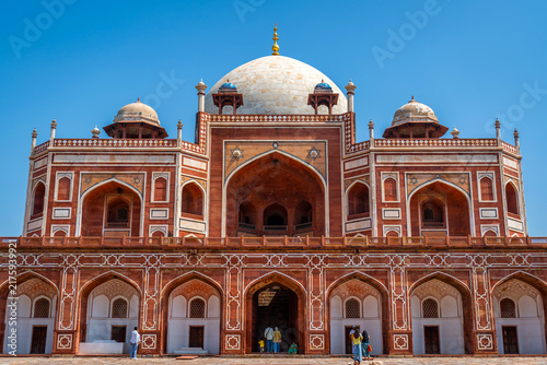Symmetrical view of the grand red sandstone mausoleum with white marble dome and intricate arches under a bright blue sky at Humayun's Tomb, Delhi, India.
