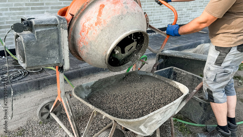 Bild auf Leinwand Construction worker using concrete mixer to pour gravel into wheelbarrow on buil