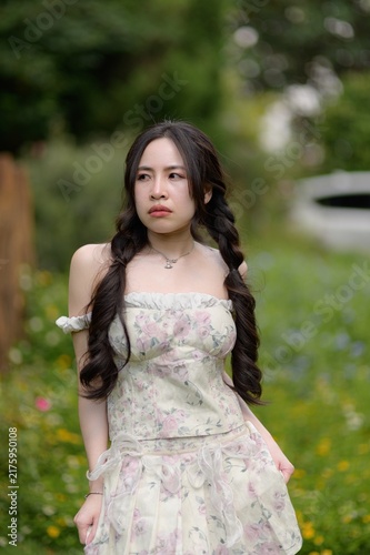 Bild auf Leinwand Young Woman Standing in Calm Garden with Flowers and Greenery