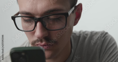 Close-up of Young Man with Glasses Focused on Smartphone with Screen Reflection