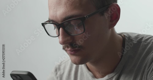Close-up of Young Man with Glasses Focused on Smartphone with Screen Reflection