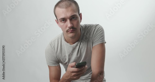 Young Man Using Smartphone and Looking at Camera on White Studio Background