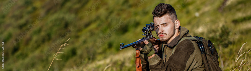 Fototapeta premium Shooter sighting in the target. The man is on the hunt. Hunt hunting rifle. Hunter man. Hunting period. Male with a gun. Close up. Hunter with hunting gun and hunting form to hunt. Hunter is aiming