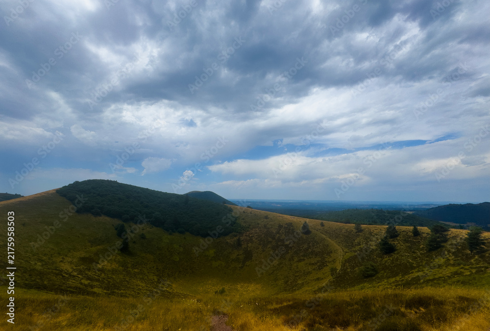 Fototapeta premium serene hills and clouds over a grassy hilltop landscape with a tranquil sky and vibrant green and blue hues in an outdoor setting, viewed from a hilltop looking out over the scenic view.