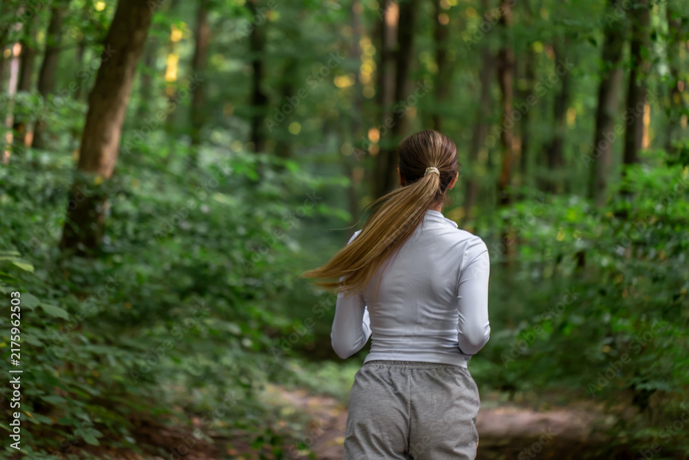 Obraz premium Woman jogging through green forest. Horizontal outdoor running scene.