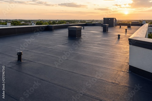 Newly completed flat roof with waterproof membrane under a golden sunset. Modern roofing system, commercial building maintenance and durable weatherproof construction concept.