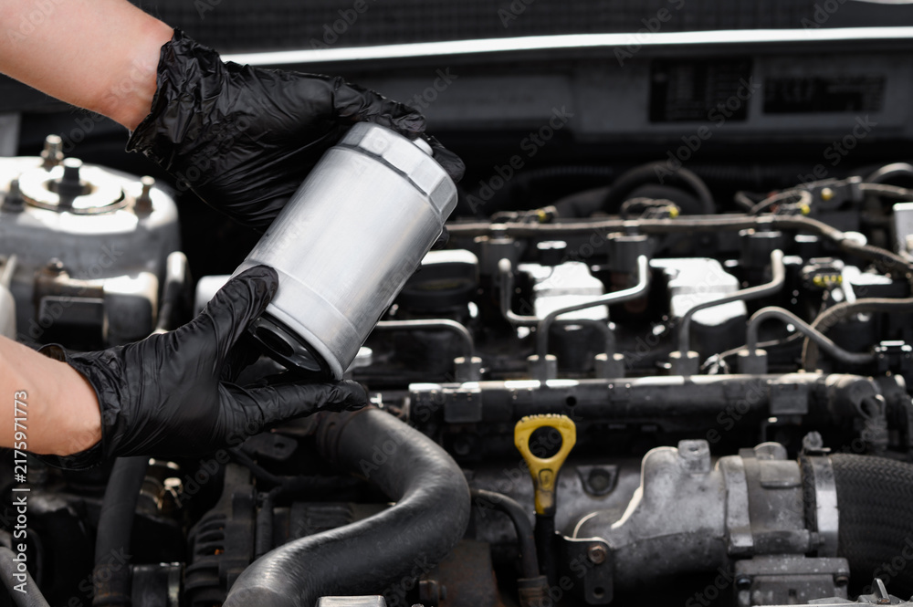 Fototapeta premium Mechanic installing new fuel filter into car engine bay close up, auto technician hands in gloves repairing vehicle, automotive service concept, professional car diagnostic, regular maintenance proces