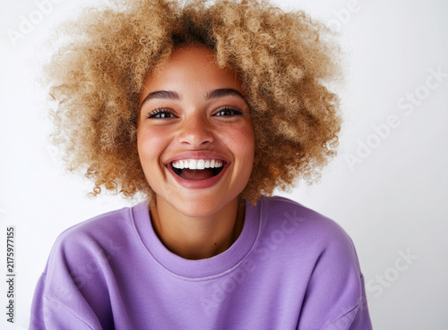 Smiling person with curly hair wearing a purple sweater against a white background