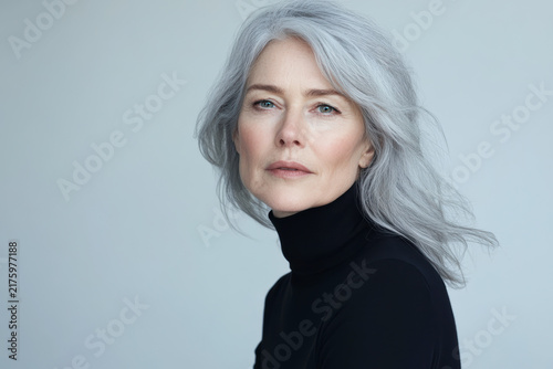 Portrait of a woman with gray hair in a black turtleneck against a neutral background