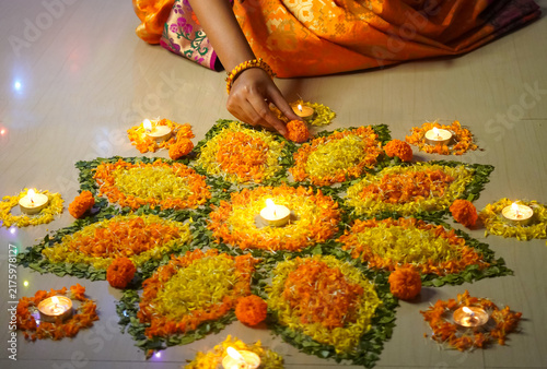 Indian Diwali preparation at home. Woman arranging flower rangoli with diyas, and colored flowers, creating a festive & spiritual atmosphere. Perfect for culture preparation.