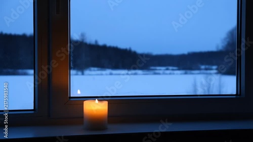 Cozy Candle Burning on Windowsill with Snowy Winter Landscape View at Twilight