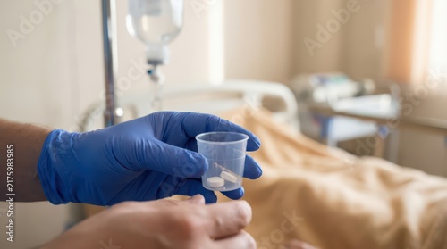 Closeup of gloved hands preparing pills in a plastic cup at bedside for hospice and palliative care medication administration and nursing procedure