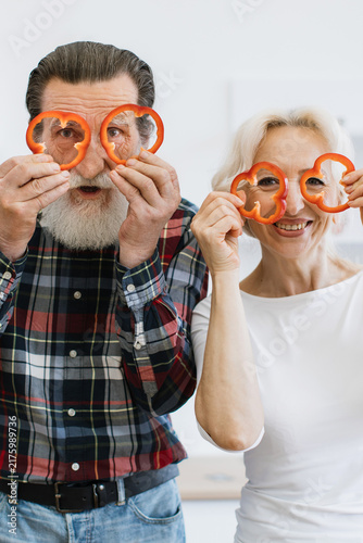 фотографія An elderly couple playfully holds slices of red bell pepper over their eyes, sha