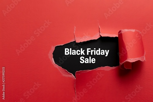 Black friday sale text revealed through a hole torn in bright red paper background for retail promotion