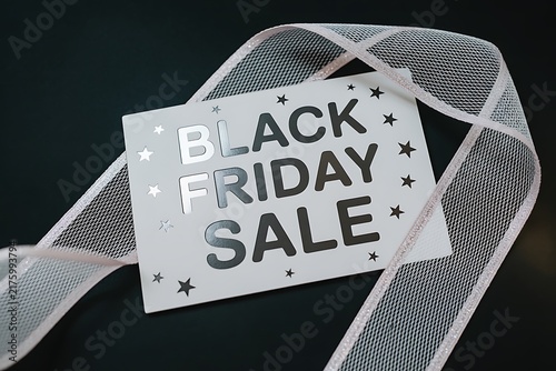 A white gift tag with black friday sale text attached to a decorative silver ribbon on black background
