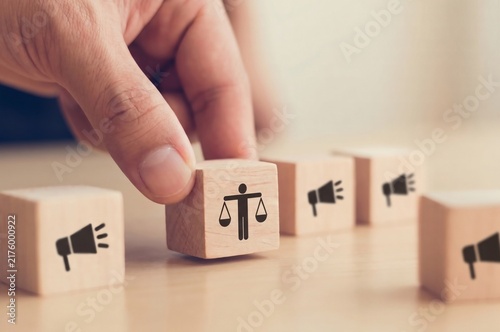 Legal justice and corporate ethics, hand placing wooden block with scales of justice icon to promote fair business practices and social responsibility.