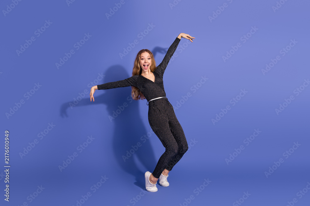 Fototapeta premium Young stylish woman in striped jumpsuit dances and smiles against a violet background for lifestyle fashion advertising and retail styling