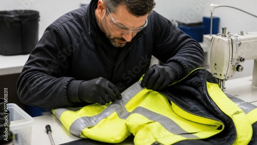 Reflective work jacket repair: A safety-gear technician replaces a damaged reflective strip on an unbranded high-visibility jacket