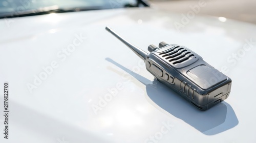 Portable two-way radio walkie-talkie lying on white car hood. Wireless communication device for security, police and emergency services. Radio transmitter concept.