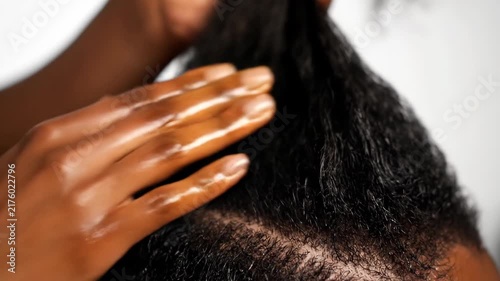 Black woman applying nourishing oil to natural curly hair. Close-up of hands massaging a moisturizing treatment into the scalp. Ethnic hair care routine