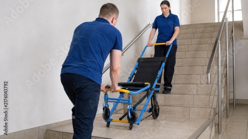 Wheelchair evacuation chair drill: Trained staff practice transferring an empty evacuation chair down a wide stair landing before assisting anyone