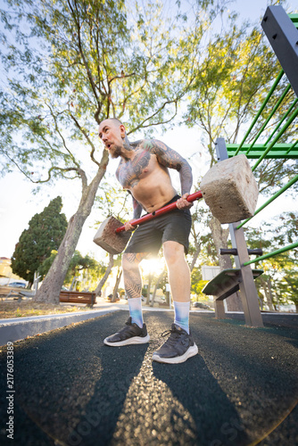 Canvas Print Man lifts heavy stones at outdoor gym during afternoon sunlight in park setting
