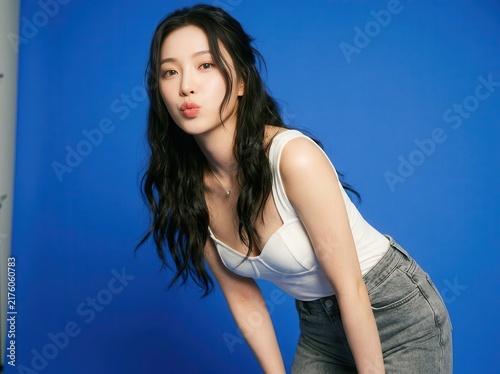 Stylish young woman in white top and denim jeans posing on vibrant blue background