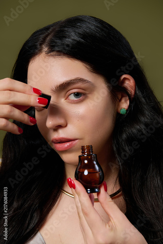 фотографія Brunette woman with long hair poses gracefully, applying serum in a chic studio
