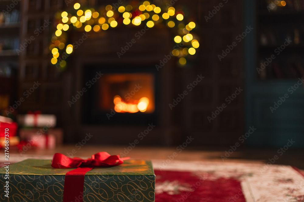 Naklejka premium Green gift box in classical Christmas decorated interior living room library with fireplace. Christmas gift near fir tree on Christmas eve. Modern classic style interior design apartment. Christmas