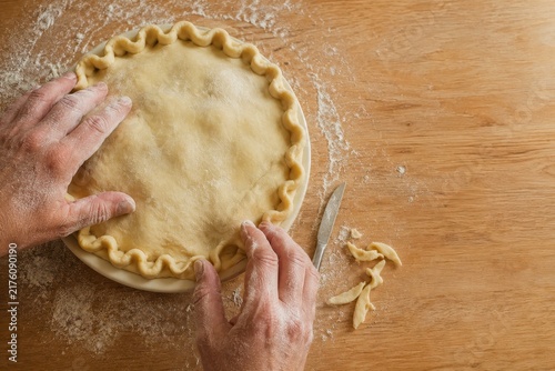 Hands crimping the edge of a pie in a ceramic dish