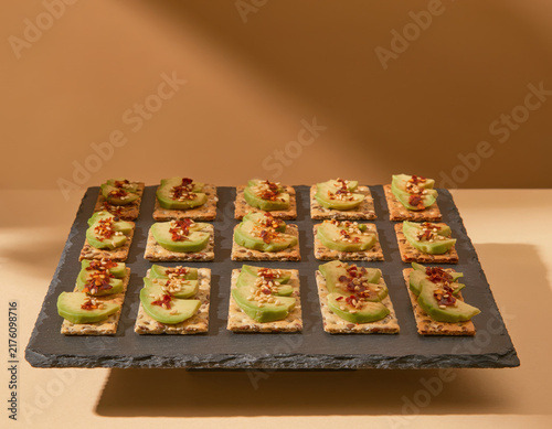 Delicious and healthy avocado crackers with sesame seeds and chili flakes elegantly arranged on a slate board, perfect for a gourmet snack or appetizer