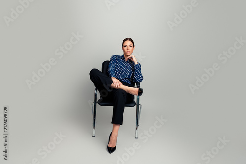 фотографія Confident professional woman seated cross-legged in chair wearing polka dot blou