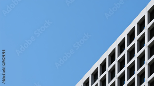 The geometric grid facade of a white modern building appears in the bottom right corner against a pure cloudless blue sky.