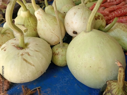 Konstfotografi A close-up view of freshly harvested light green gourds displayed on a blue market stall surface, with other vegetables in the background