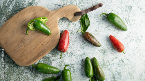 Fotografie Green and red jalapeno chili peppers on green and white surface.