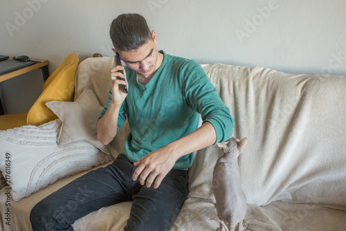 Bild auf Leinwand A young man sits on a couch holding his phone