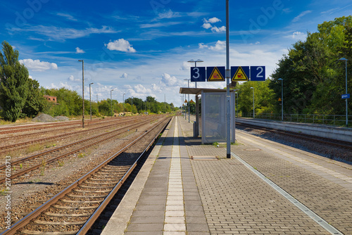 Blick über den leeren Bahnsteig und die weitläufigen Gleisanlagen des Bahnhofs an einem sonnigen Sommertag, Salzlandkreis, Sachsen-Anhalt, Deutschland