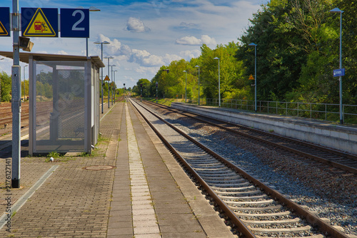 Blick über den leeren Bahnsteig und die weitläufigen Gleisanlagen des Bahnhofs an einem sonnigen Sommertag, Salzlandkreis, Sachsen-Anhalt, Deutschland