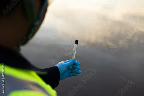 Environmental technician inspecting a clear water sample in a test tube beside a lake.