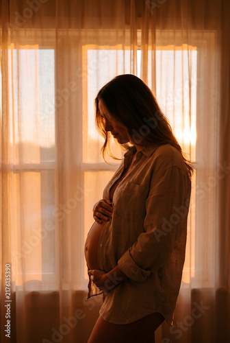 Pregnant woman standing by window in golden sunlight