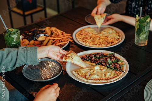 Diners share assorted pizzas, fries, fried snacks and refreshing mint drinks around a wooden restaurant table