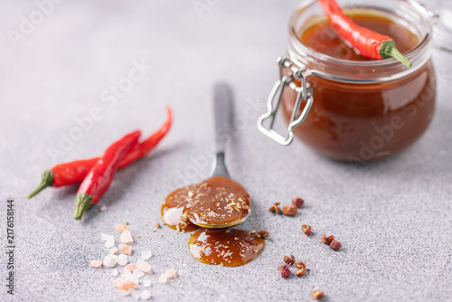 Glass jar with salted caramel with chili pepper on grey background. Trendy swicy food