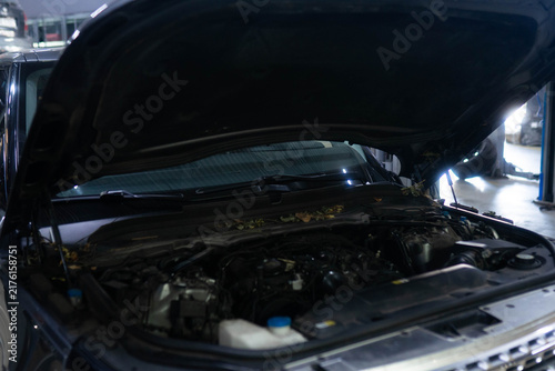 Open hood reveals engine bay inside repair garage for inspection. Technician checks hoses and caps recording condition for service log