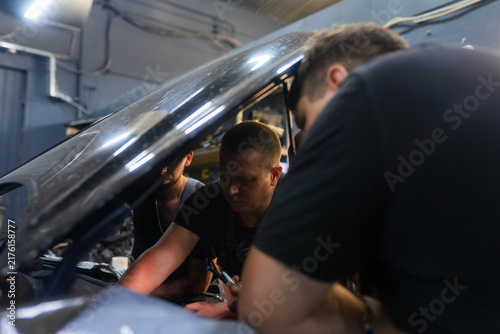 Cuadro en lienzo Garage workers gather around faulty automobile with open bonnet