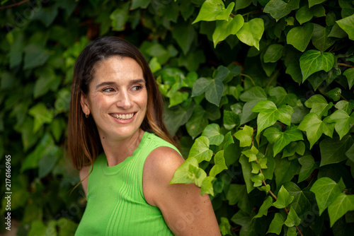 Brunette woman smiling naturally in front of green ivy wall