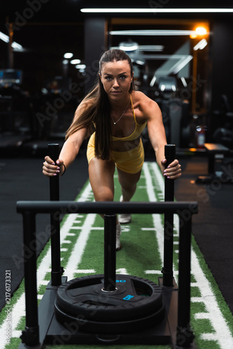 Fotografie Focused woman pushing weighted sled on gym turf track