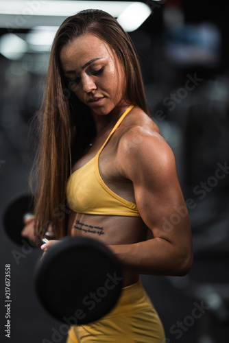 Fotografie Dimly lit gym with fit woman in yellow sportswear focused on performing dumbbell