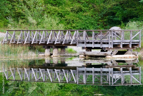 Фотография Passerelle en bois parfaitement reflétée dans l’eau calme d’un étang